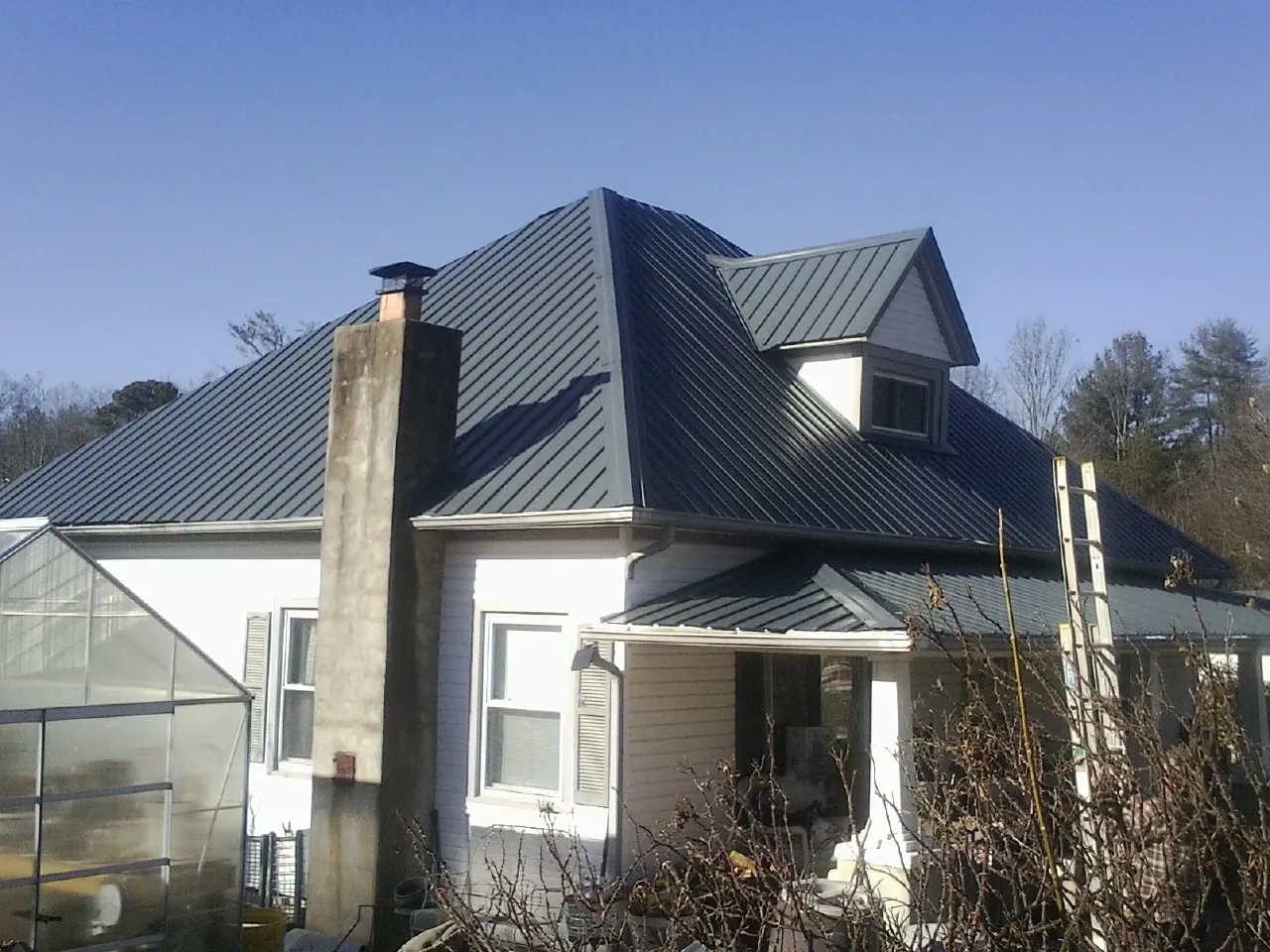 Dark blue standing seam metal roof on a white farmhouse with dormer — Slate & Tile Roof Repair by Roofing Brothers in Jessieville