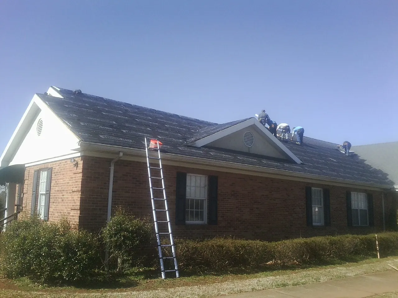 Crew tearing shingles off a brick ranch roof with a ladder set — Metal Roof Repair work by our crew in Jessieville