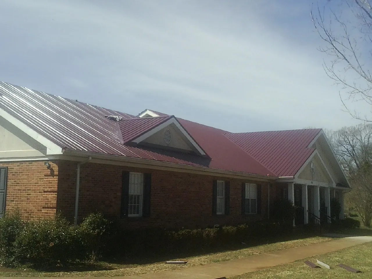 Red metal roof with gabled entries on a long brick building, from a Hail Damage Roof Repair job in Jessieville