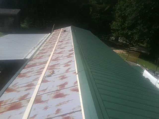 Old rusted panels beside newly installed green metal roofing — Wind Damage Roof Repair by Roofing Brothers in Jessieville