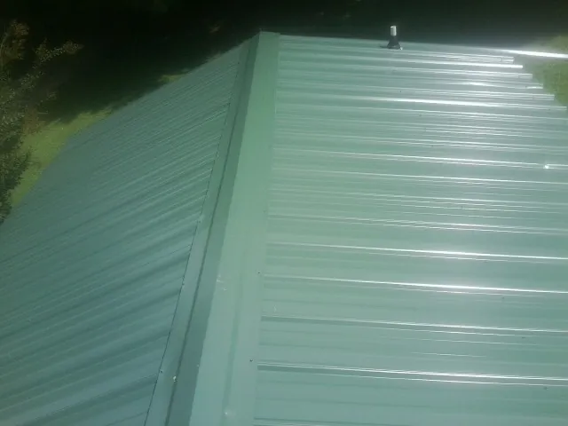 New green metal panels meeting at the ridge of a roof — Flat Roof Repair work by our crew in Jessieville
