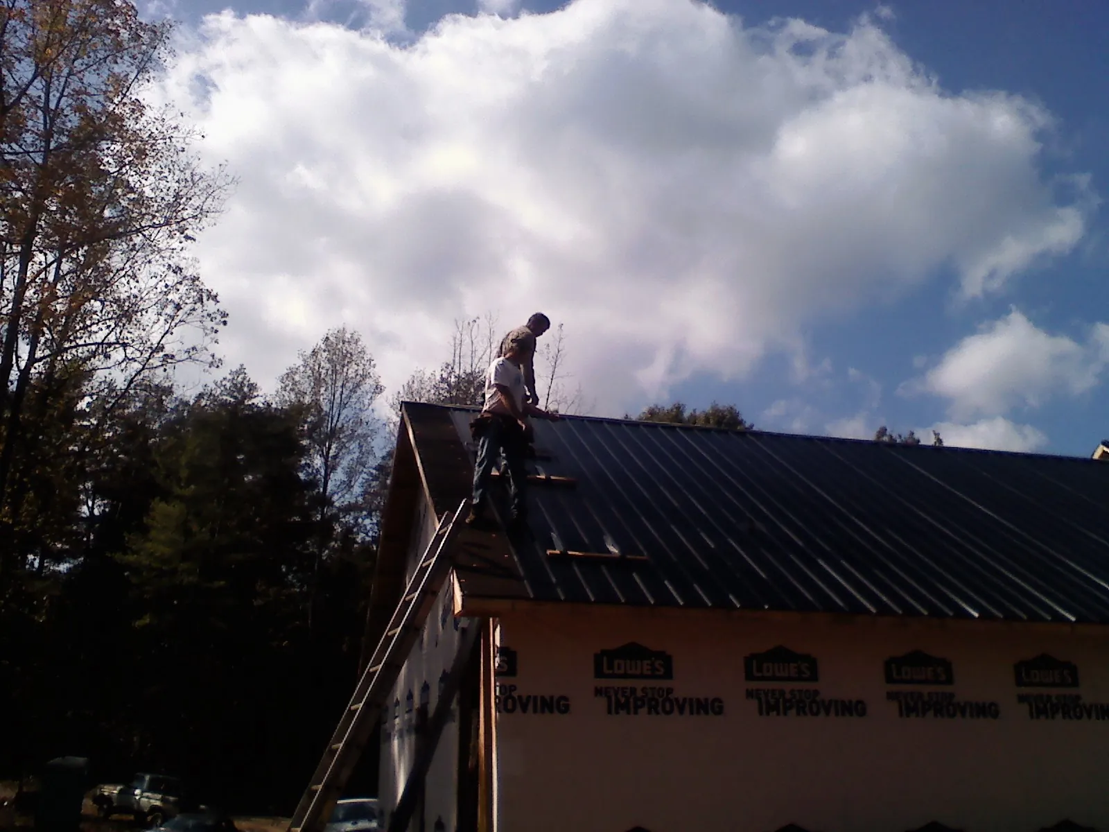 Roofer fastening dark metal panels high against a cloudy sky, from a Roof Inspection job in Jessieville