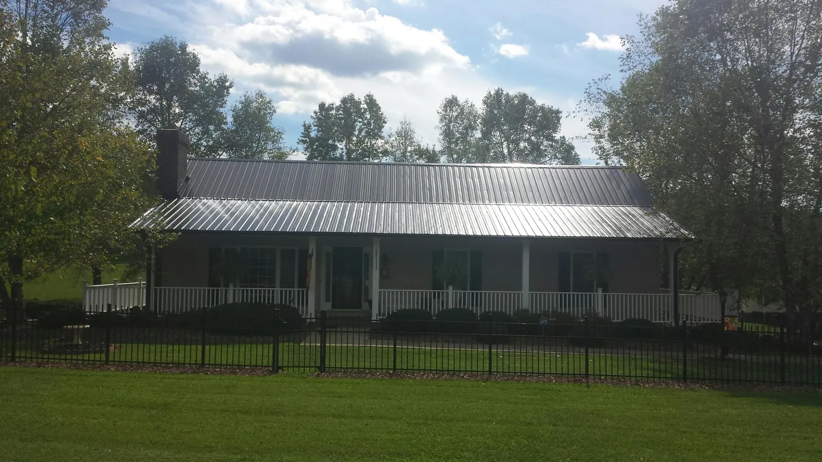 Gray metal roof on a brick ranch with a full width front porch — Gutter Guard Installation work by our crew in Jessieville