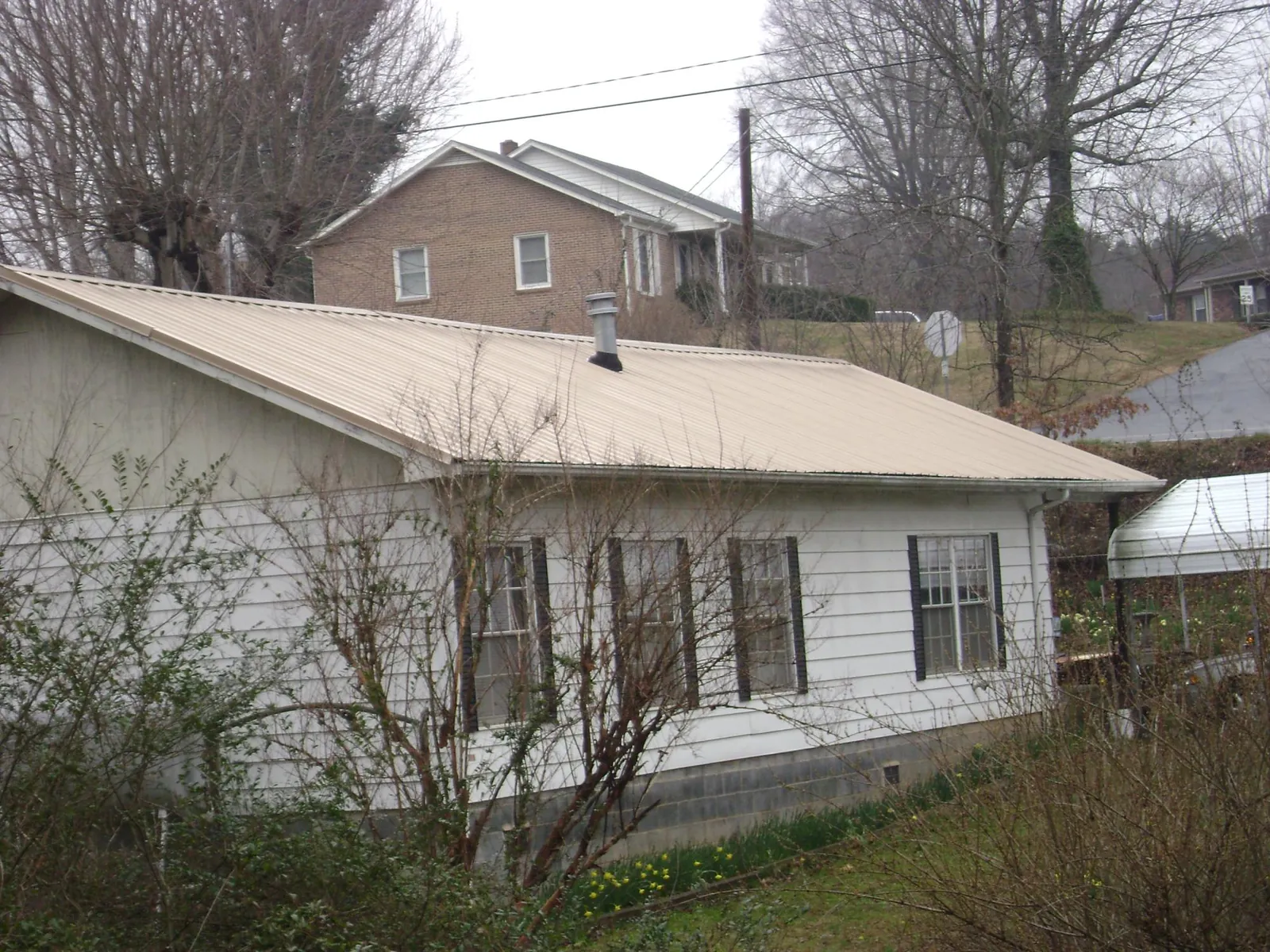 Tan metal roof on a white sided house set into a hillside — Commercial Roofing by Roofing Brothers in Jessieville