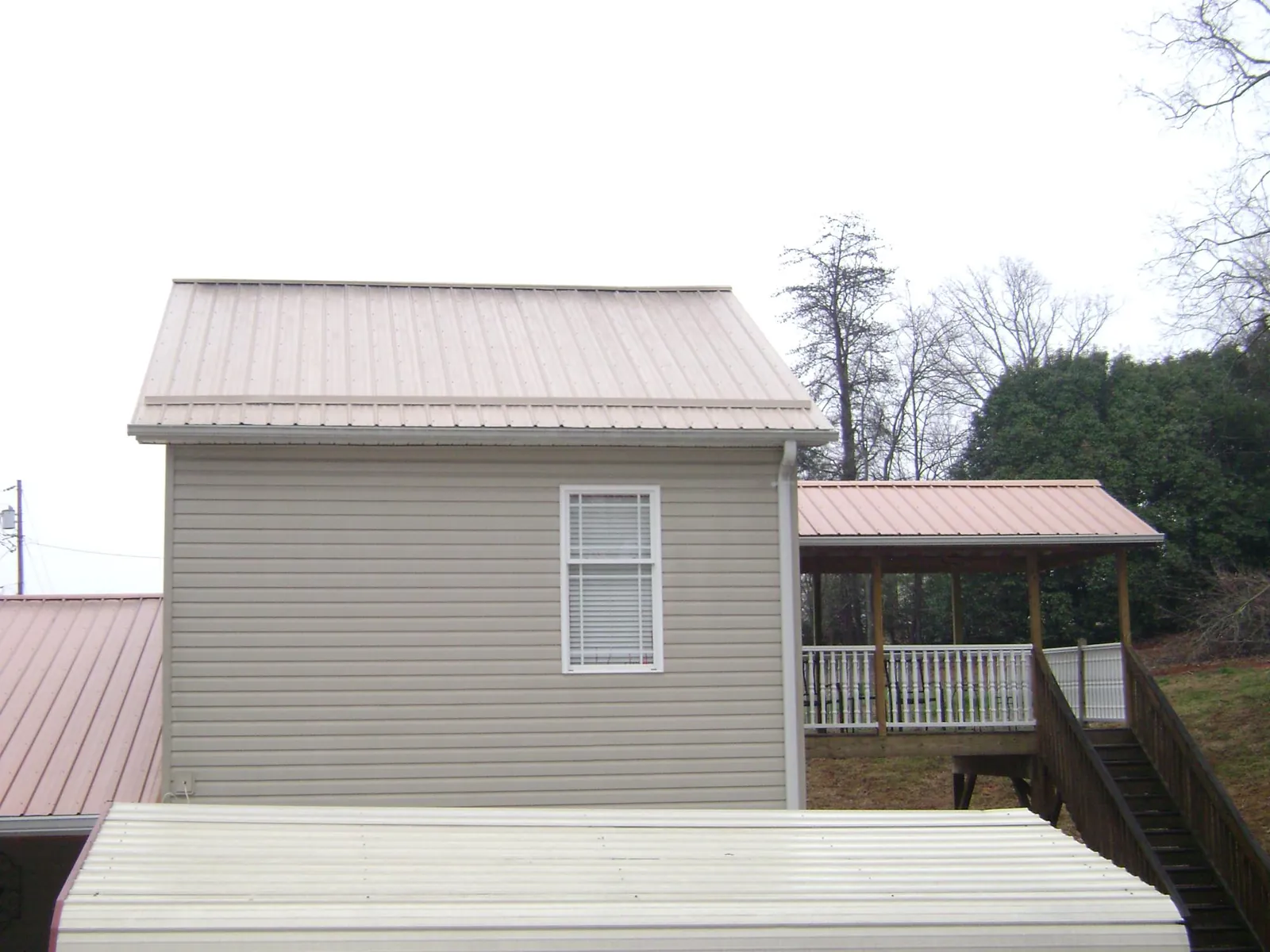 Tan metal roofs on a two story addition and attached porch, from a Roof Replacement job in Jessieville